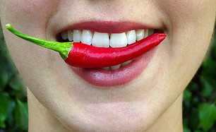 Woman smiling with a red chill in between her teeth. 