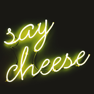 Yellow neon sign: "Say Cheese" against a black background. 