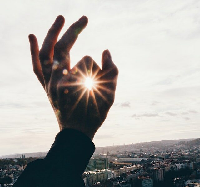 Hand held up closing fore finger and thumb around the sun. 