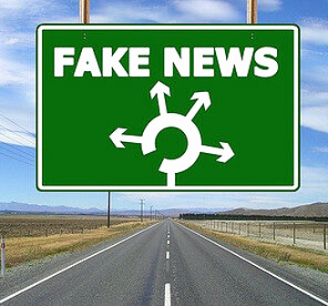Green road sign with a roundabout and the words fake news atop. 