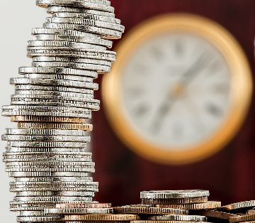 A stack of silver coins with a clock blurred in the background. 
