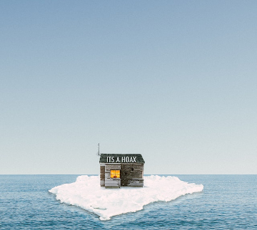 A wooden shack on a melting ice sheet drifting off into the sea with a sign on the door reading, It's a Hoax! 