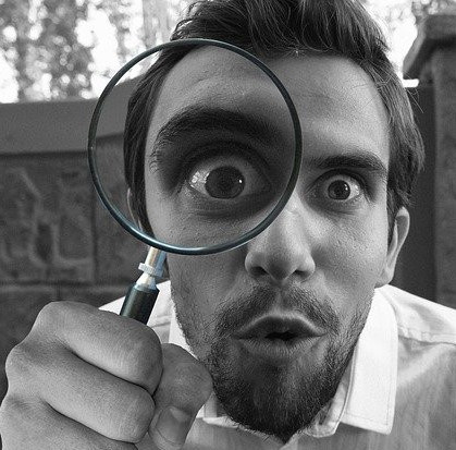 Man looking through a magnifying glass with a surprised expression on his face.