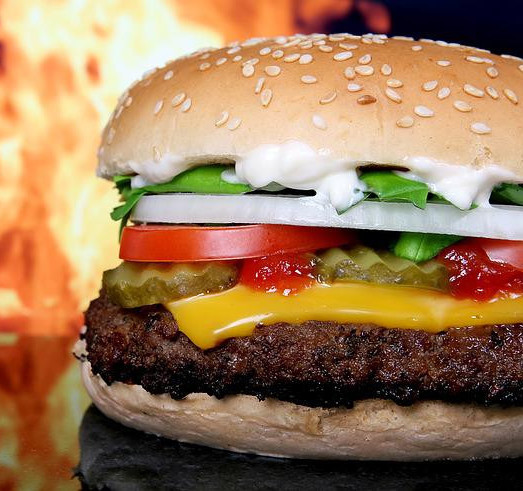 A big dirty burger with flames in the background. 