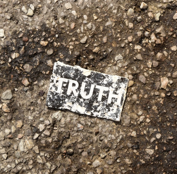 Battered old badge lying on the tarmac with the word truth on there.