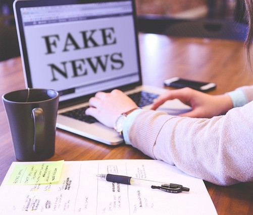 Person working at the laptop with the words 'fake news' on the screen.