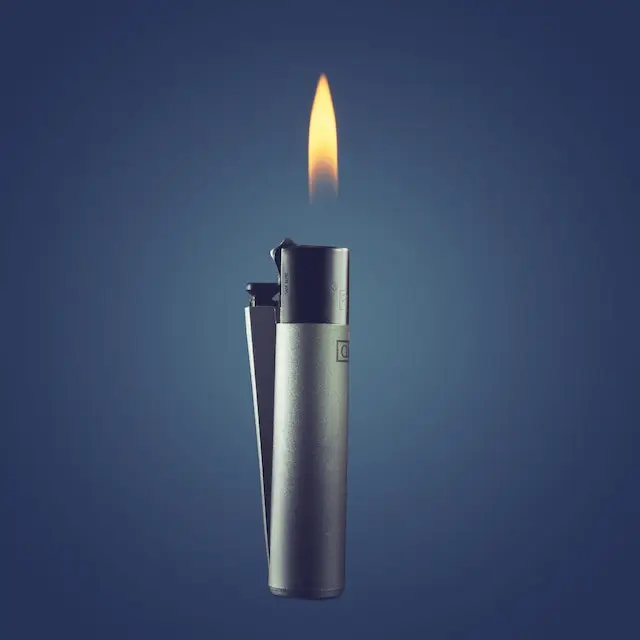 A clipper lighter with the flame on, against a blue background. 