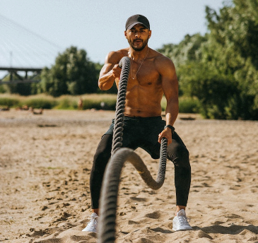 Man on the beach exercising with the battle ropes. 