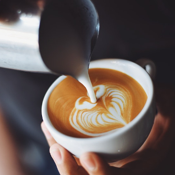 Close up of a barista pouring oat milk into a cup of coffee. 