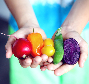 Holding various coloured vegetables in her hands. 