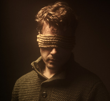 Man blindfolded with lengths of rope. 