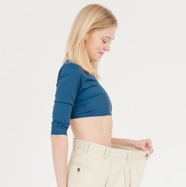 Woman holding open her over-sized trousers to show how she lost weight. 