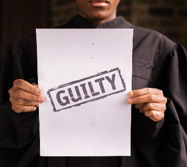 Woman holding up a piece of A4 paper with the word 'Guilty' on it. 