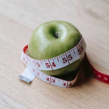 A green apple with a tape measure around it. 