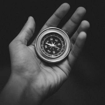 A black and white image of a person's open hand holding a compass. 
