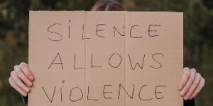 Demonstrator holding up a cardboard sign with the words 'Silence Allows Violence".