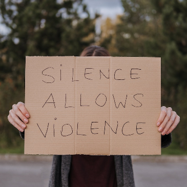Demonstrator holding up a cardboard sign with the words 'Silence Allows Violence". 