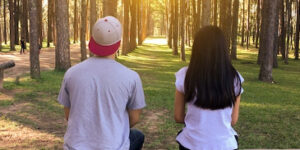 A young couple with their backs to the camera looking out over a wooded landscape.