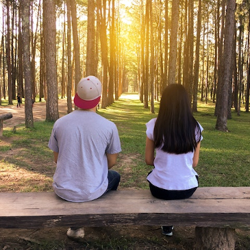 A young couple with their backs to the camera looking out over a wooded landscape. 