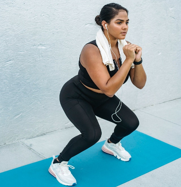 Woman with earbuds in doing squats on her yoga mat. 