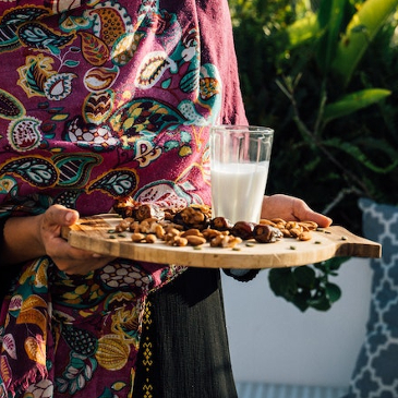 Woman holding a wooden chopping board with a selection of nuts and a glass of almond milk on there. 