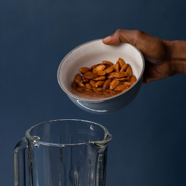 Pouring a bowl of almonds into a blender to make home made almond milk. 