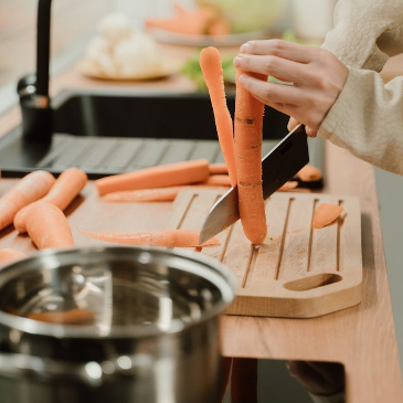 Close up of a carrot on a chopping board being sliced down the middle. 