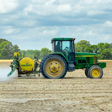 A tractor with sprayer applying chemicals to a ploughed field.