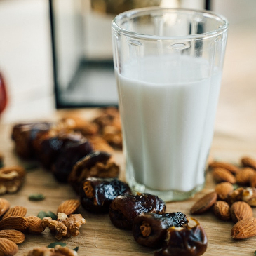A glass of almond milk set against a backdrop of almonds and dates on a chopping board.