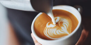 A barista pouring almond milk into a cappuccino to make a heart shape.