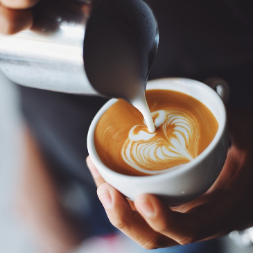 A barista pouring almond milk into a cappuccino to make a heart shape.