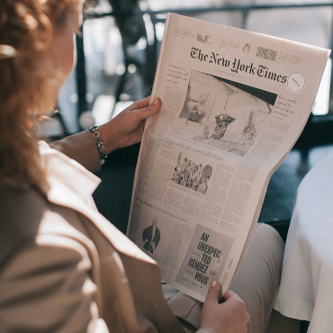 A photo taken over the shoulder of a woman reading the New York Times. 