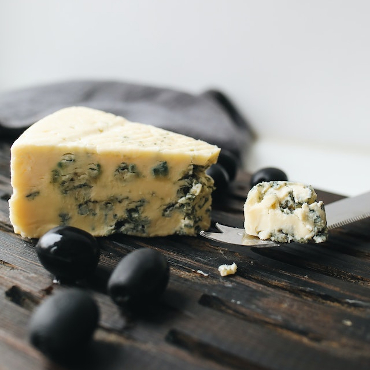 A wedge of blue cheese on a cheese board with some black olives. 