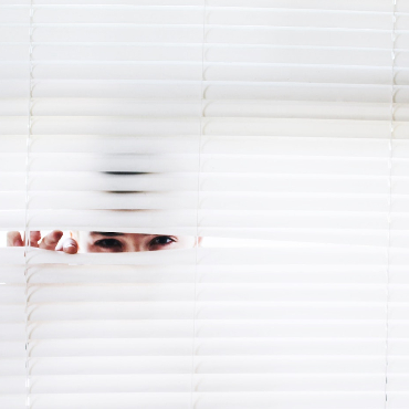 Man peeking through white Venetian blinds. 