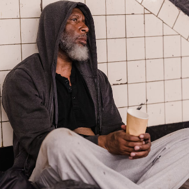 A desperate looking homeless man holding a paper cup. 