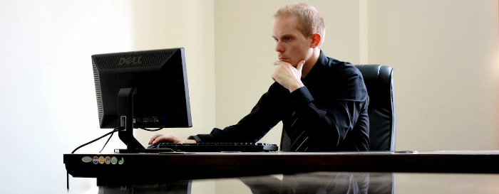 Man in a black shirt staring intently at the computer screen. 