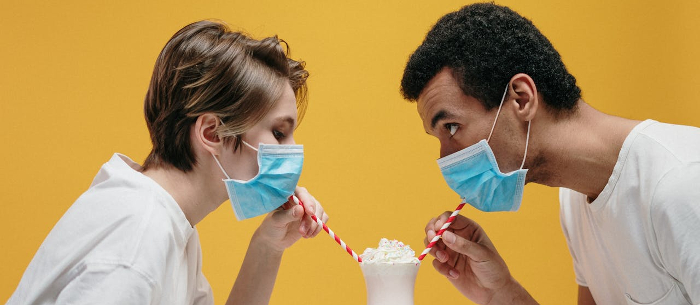 Two nurses with masks on trying to share a milkshake using straws 