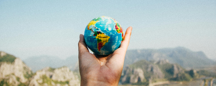 Person holding a small globe model of the Earth with a hot looking terrain in the background 