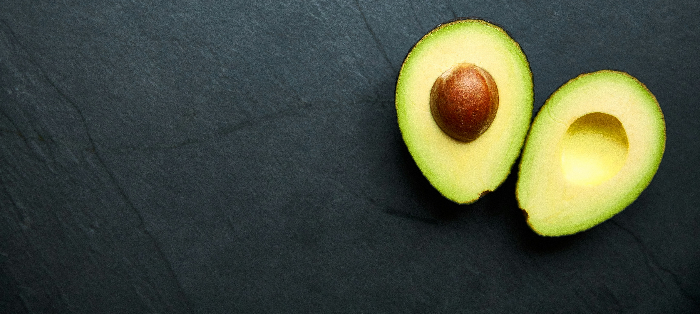 An avocado sliced in half against a slate background. 