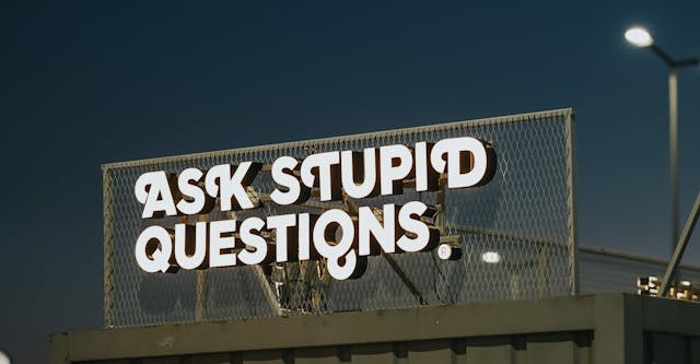A sign above a shop reading "Ask Stupid Questions" 