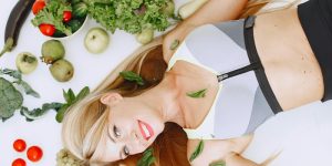 Healthy looking woman lying on the floor with veggies scattered around her.